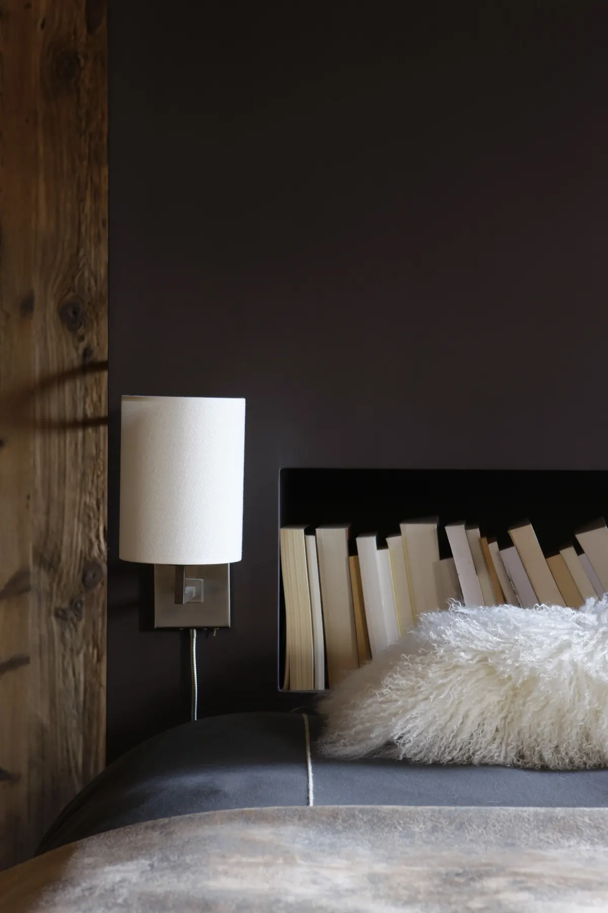 Tête de lit en bois flotté, lampe et fourrure dans une chambre sombre