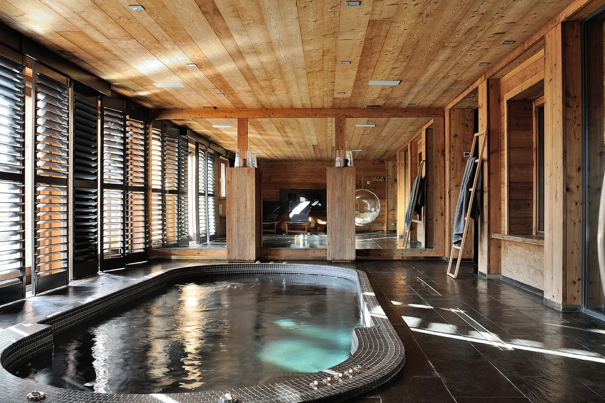 Piscine intérieure chauffée sous un plafond de bois, baies vitrées à volets