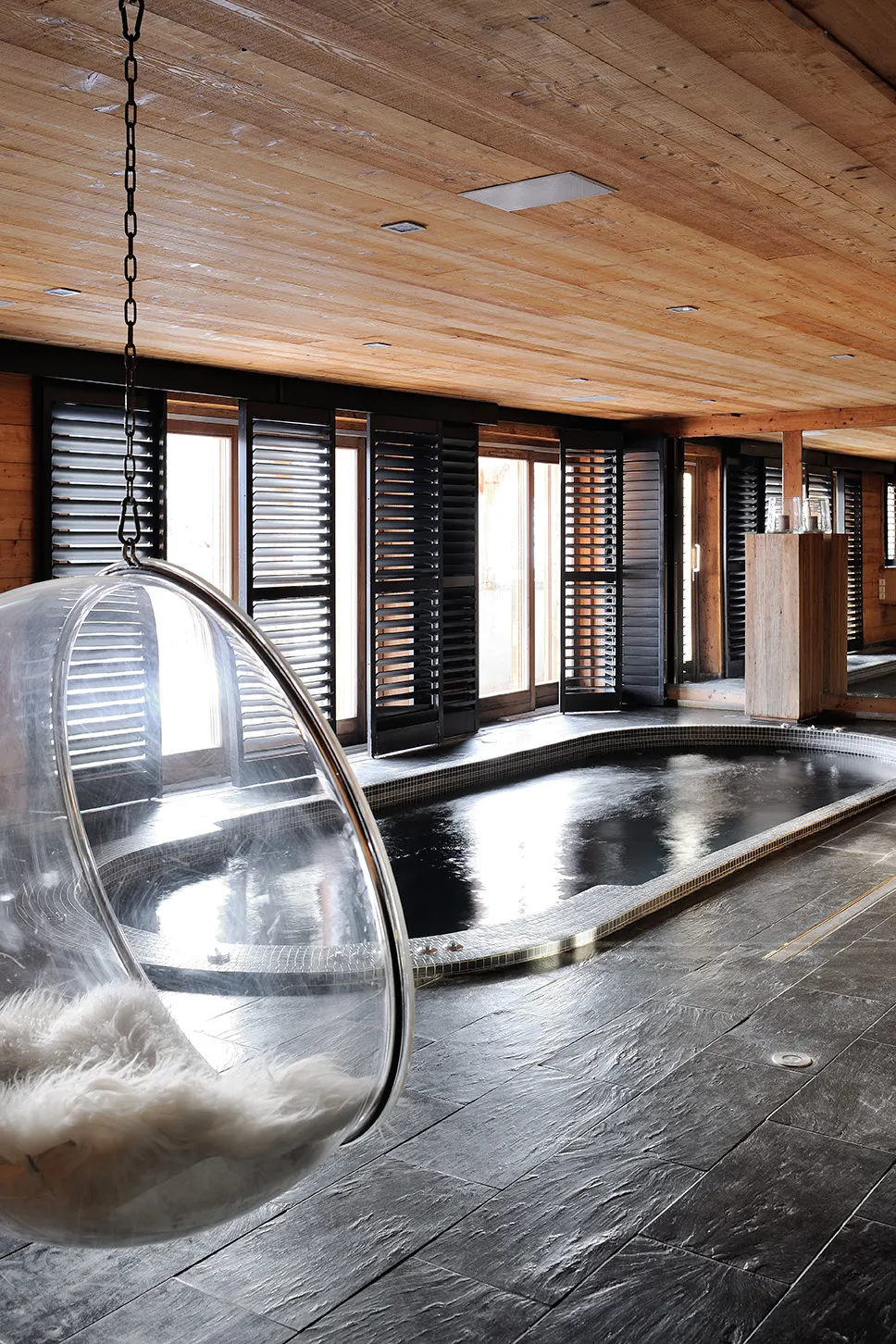 Fauteuil bulle suspendu au bord de la piscine intérieure du chalet