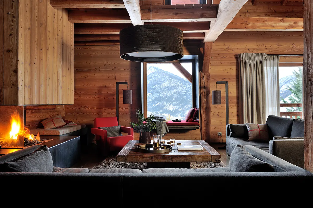 Grand salon du chalet, feu dans la cheminée vitrée et canapés face à la vallée